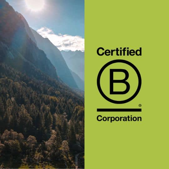 A stunning aerial view of a forested mountain valley with sunlight breaking through the peaks, alongside the Certified B Corporation logo.