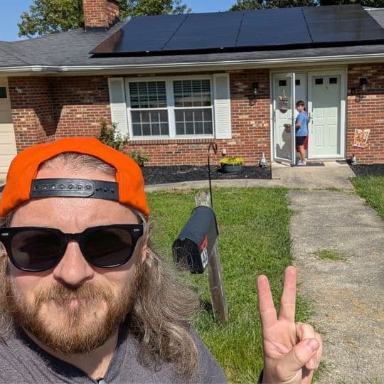 A member pointing to his house with solar panels behind him.