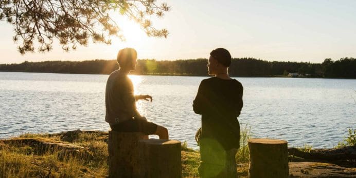 The image shows to men sitting near a river at sunset.